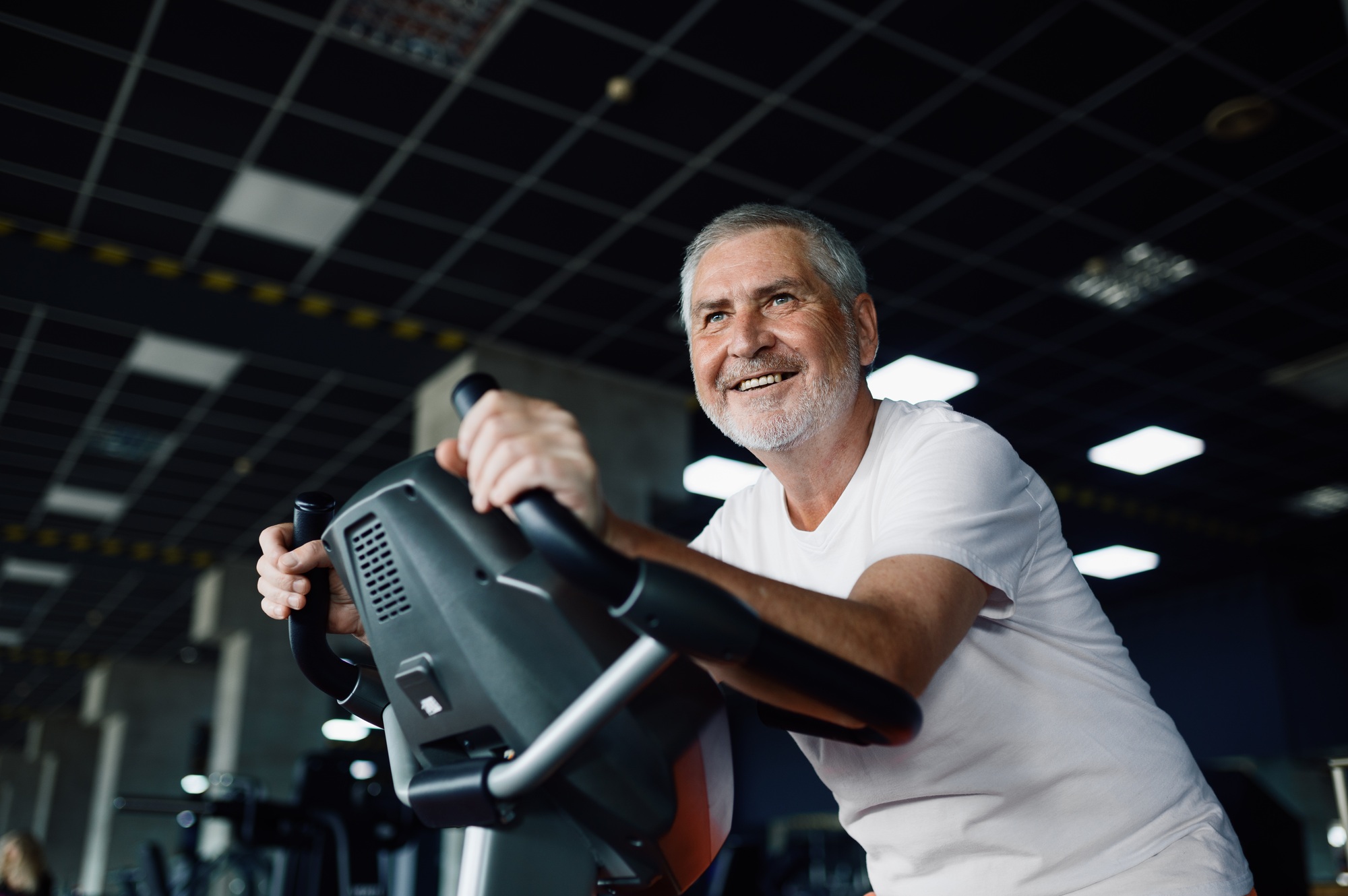 Elderly man poses on exercise bike in gym