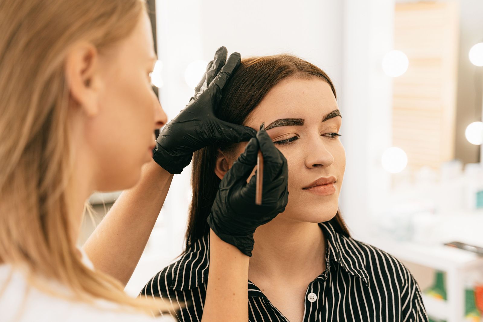 Aesthetician shaping a client’s brows with a brush in a bright treatment room