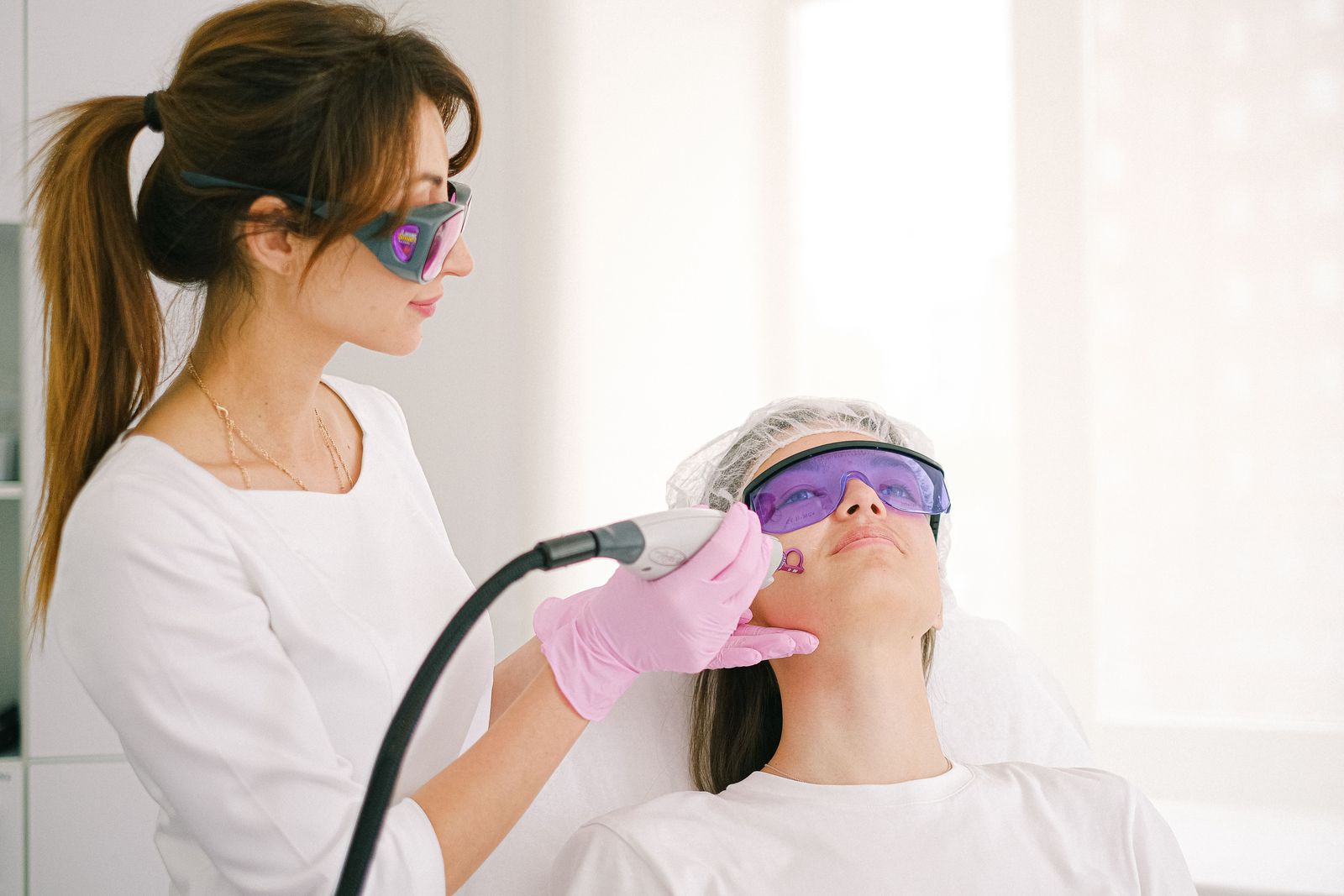 Aesthetician guiding an IPL handpiece across a guest’s cheek in a bright treatment room