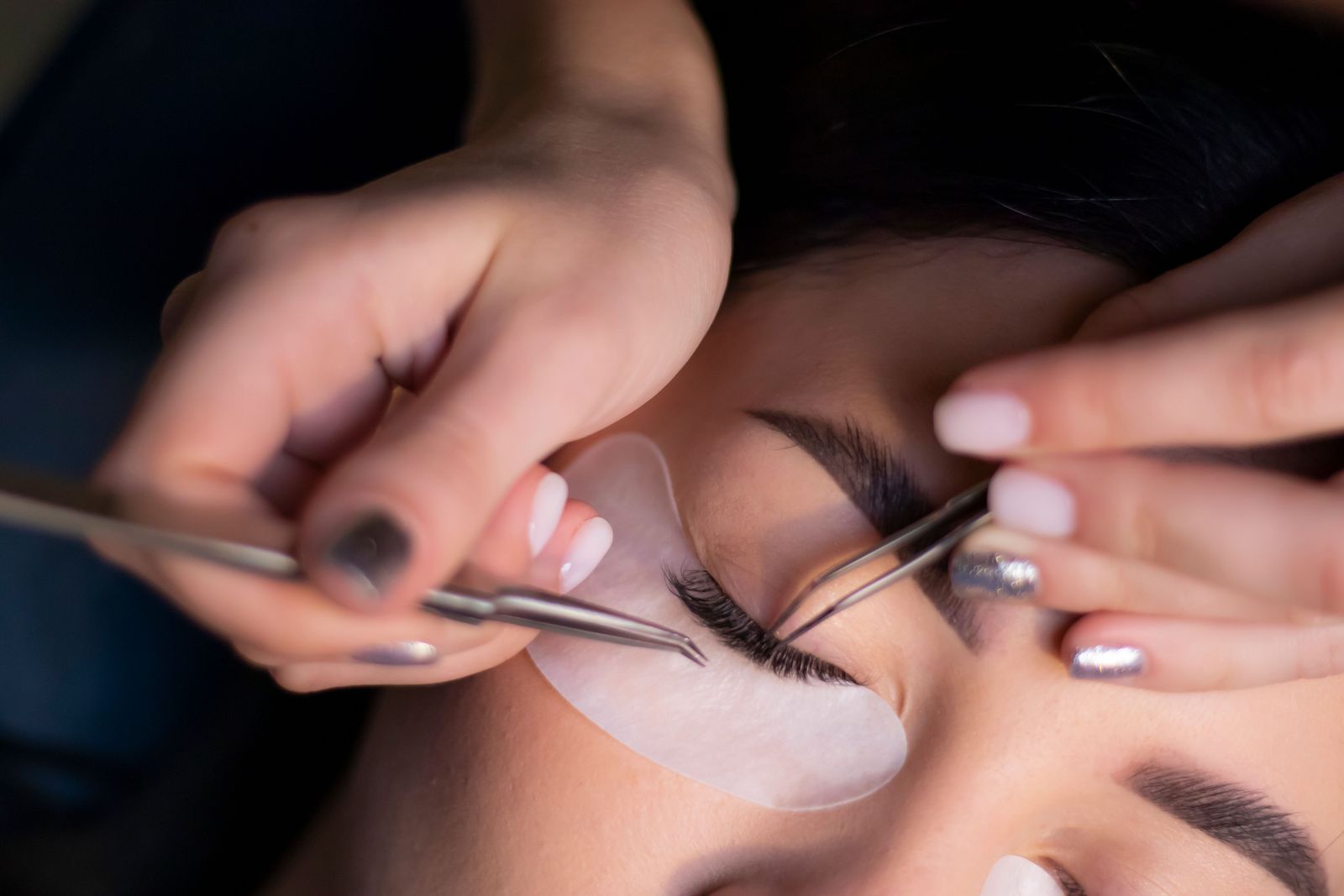 Aesthetician shaping lashes over a protective under-eye pad during a lash lift appointment