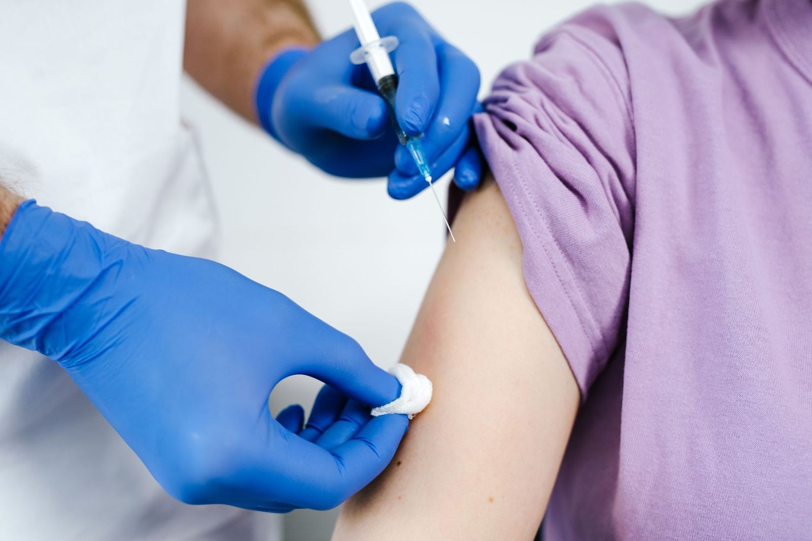 Gloved hands preparing an injection in a patient's upper arm