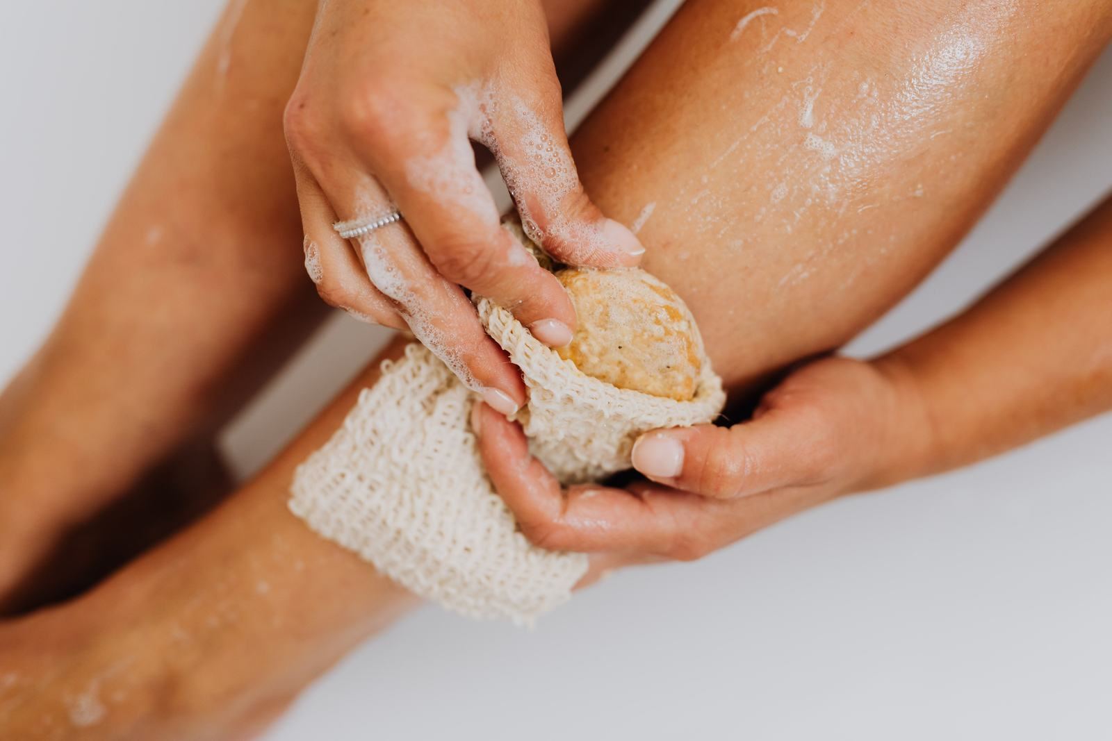Close-up of hands using an exfoliating mitt on a leg during a shower
