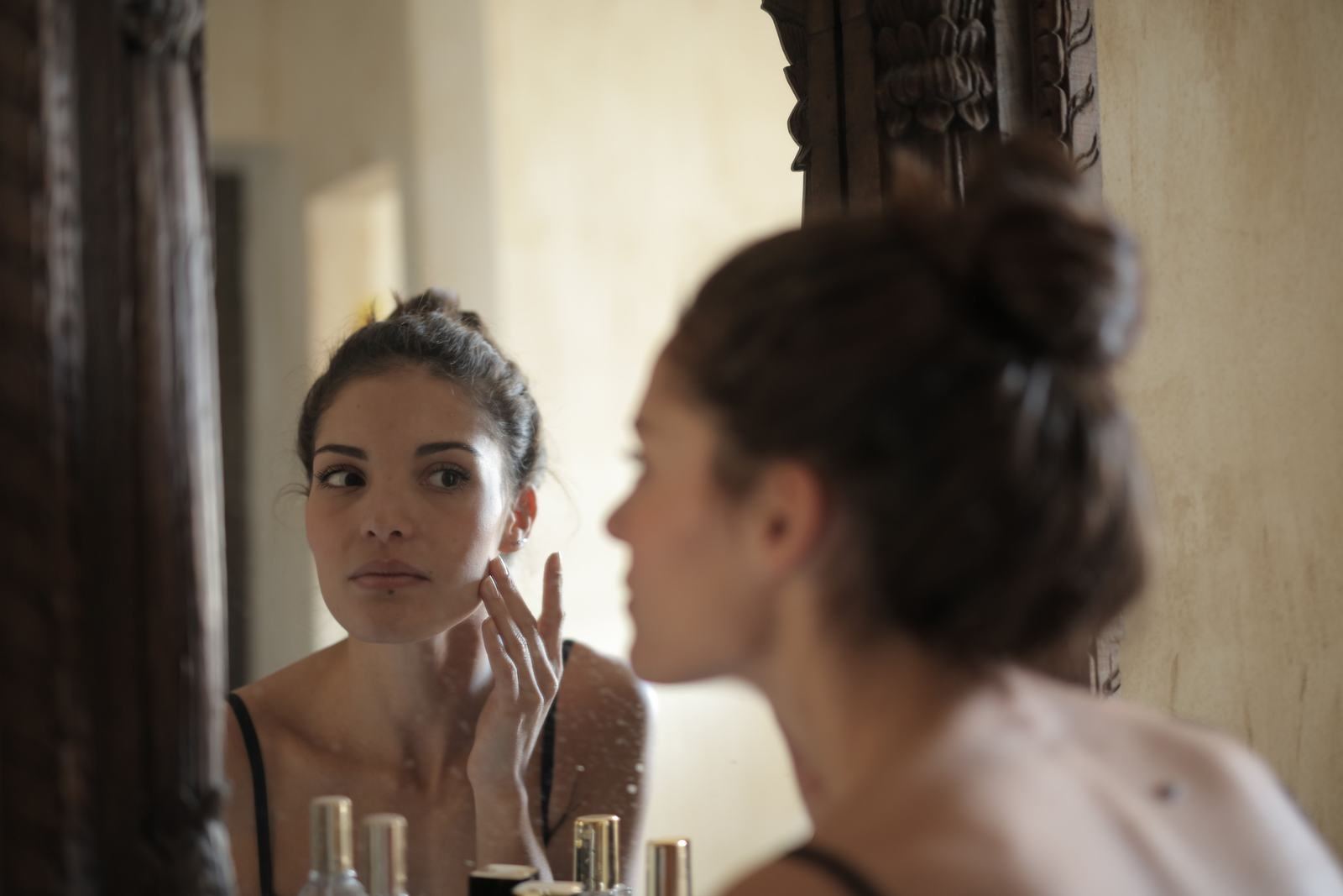 A woman looking at her reflection in a mirror with her hand resting lightly on her cheek